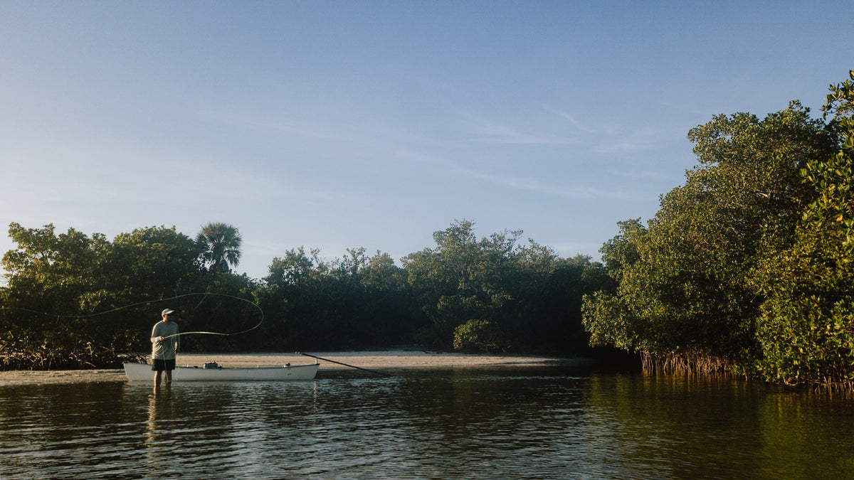 a photograph of commercial fly tier and professional photographer Josh Idol casting a fiberglass fly rod in a narrow creek in the Ten Thousand Islands near Everglades National Park. his canoe is staked out in the background.